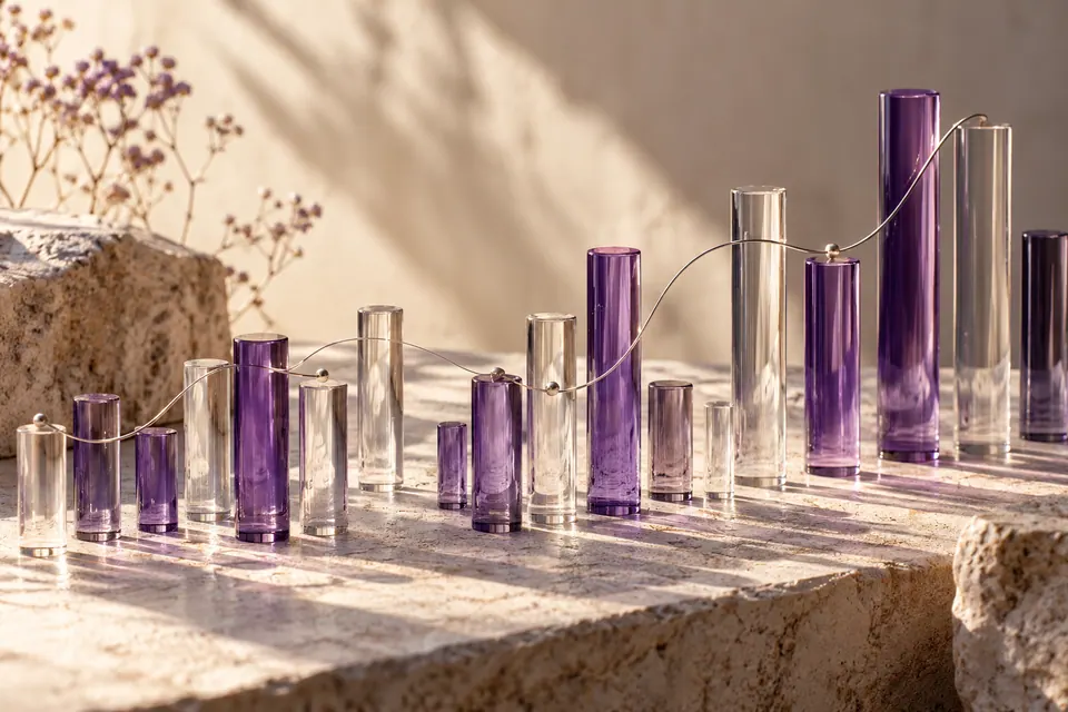 Neat rows of translucent violet and clear glass rods of varied heights, a single curving silver thread connecting selected rods